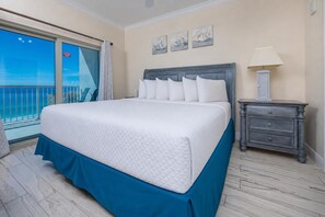 Ein Hotelzimmer mit einem großen Bett, einem Nachttisch, einer Lampe und Blick auf das Meer.