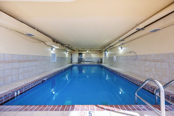Ein rechteckiger, überdachter Pool mit Fliesenrand, einer sichtbaren Tiefenmarkierung und einer Poolleiter.