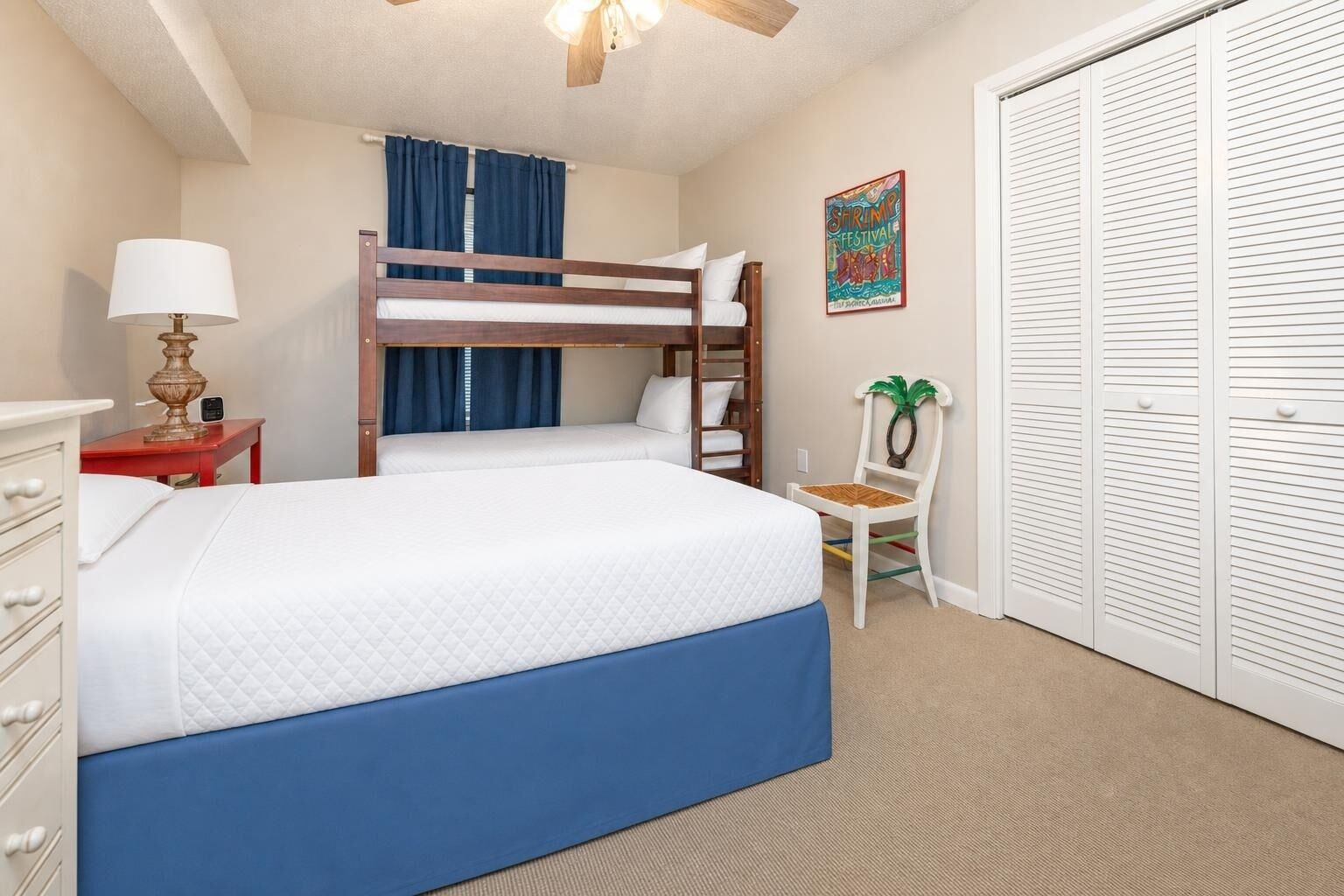 A bedroom with a bunk bed, a desk with a lamp, a chair, and a wardrobe.