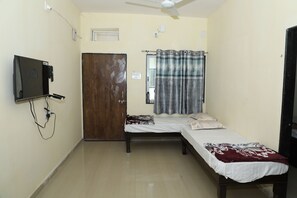 Cozy retreat with a single bed, wardrobe, and TV, complete with a ceiling fan and window with a patterned curtain.