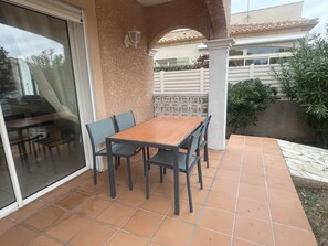 Une terrasse avec une table et des chaises en bois, une porte vitrée et une rambarde blanche.
