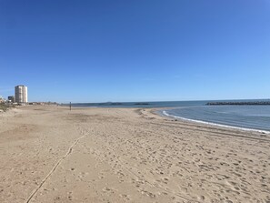 A wide sandy beach with footprints, a clear blue sky, and a distant rocky shoreline. - Valras Arrago, Maison Individuelle, Plain Pied, 6 Pers, Jardin (Valras-Plage)