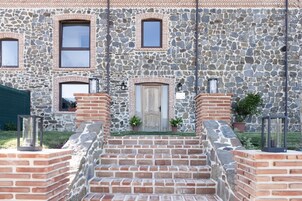 Un edificio de piedra con puerta de madera, escalones de ladrillo y dos faroles a cada lado.
