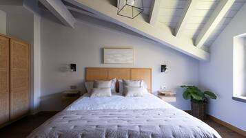 A bedroom with a large bed, wooden headboard, bedside tables, a wall-mounted light fixture, and a potted plant.