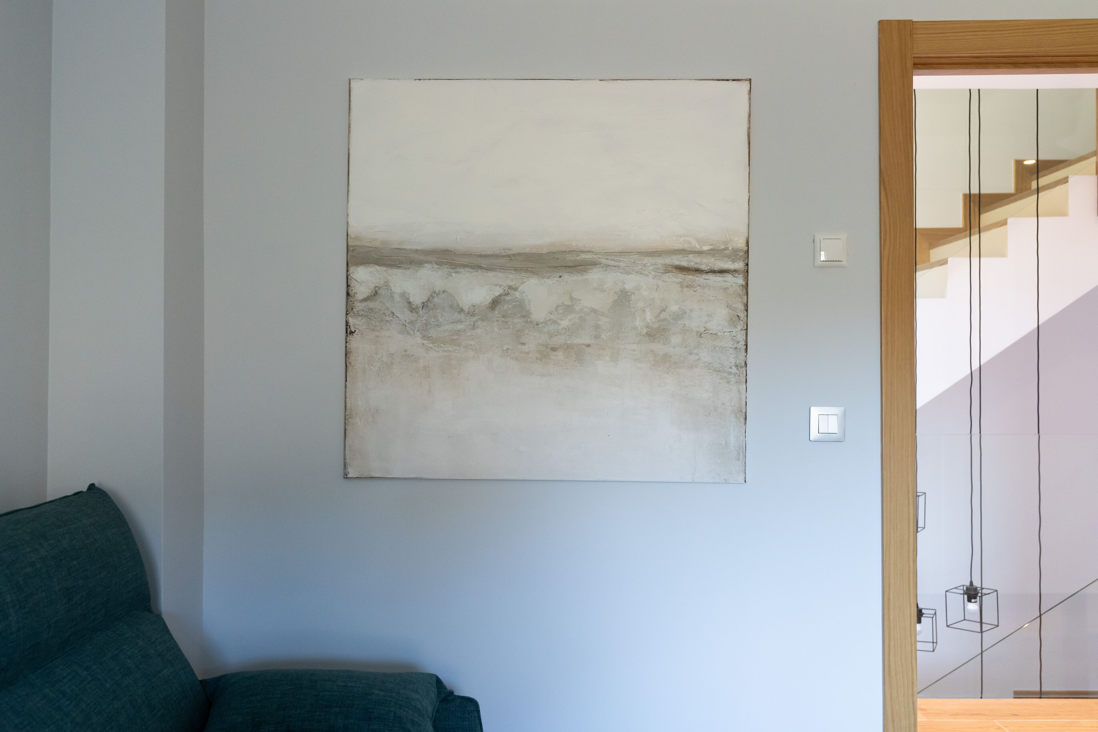 A room with a large abstract painting on the wall, a green sofa, and a staircase in the background.
