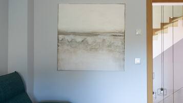 Una habitación con un cuadro abstracto grande en la pared, un sofá verde y una escalera al fondo.