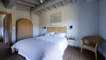 A bedroom with a large bed, wooden headboard, a wicker chair, and a painting on the wall.