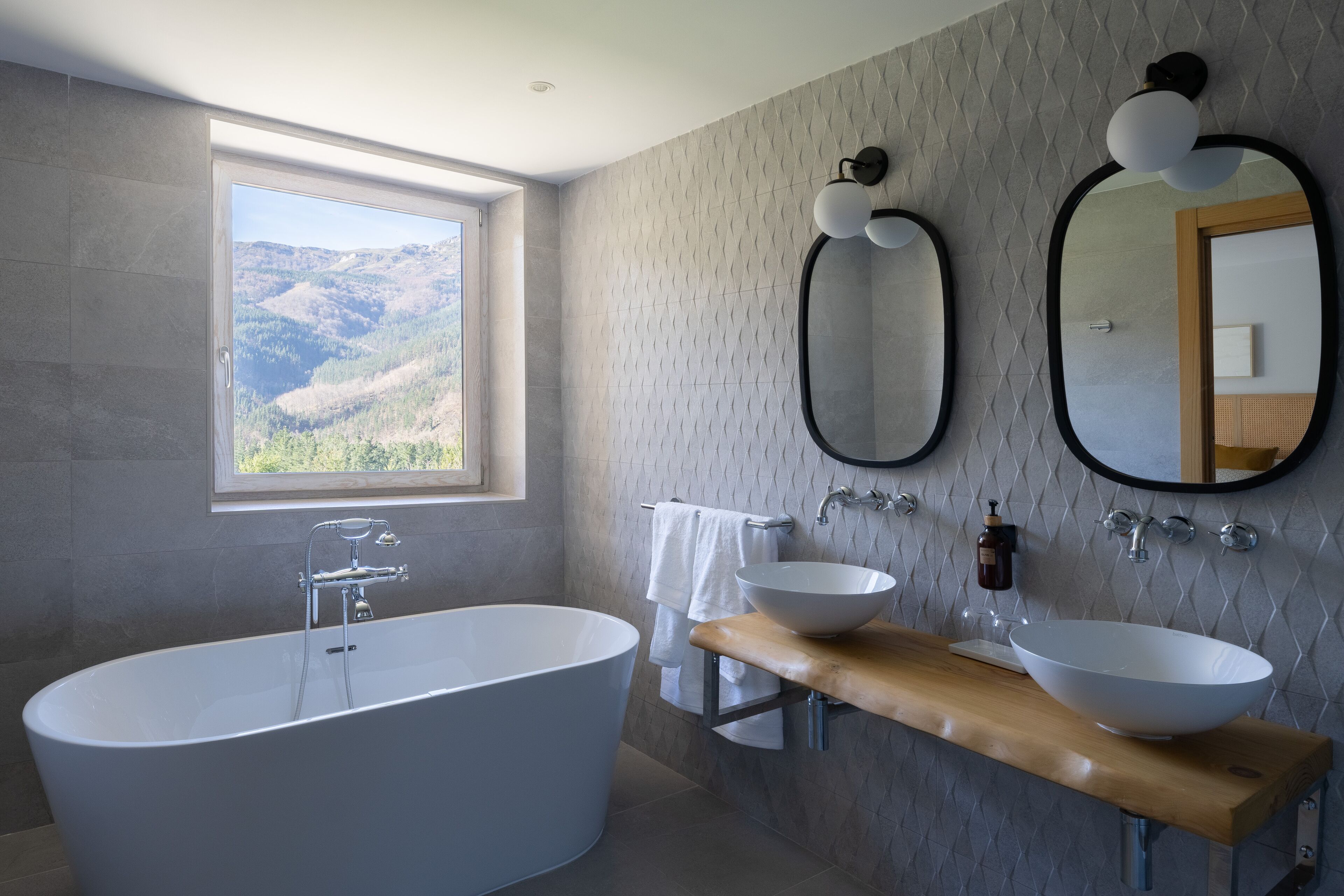 A modern bathroom with a freestanding bathtub, two large mirrors, and a wooden vanity with a vessel sink.