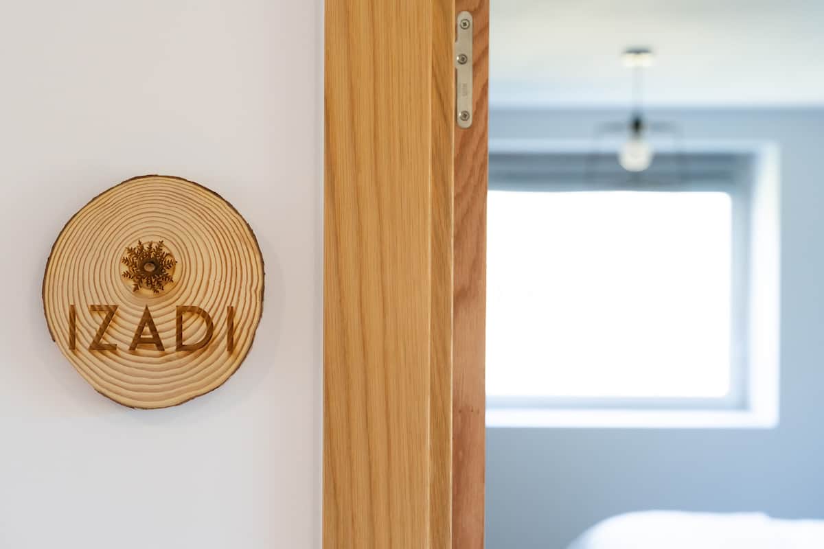 A wooden door with a metal latch and a circular wooden plaque with the name "IZADI" on a white wall.