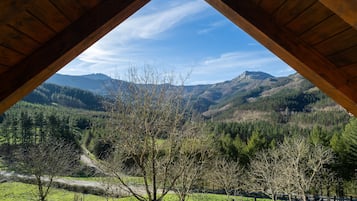 Uitzicht vanuit een kamer met houten dak op een vallei met bergen, bomen en een weg.