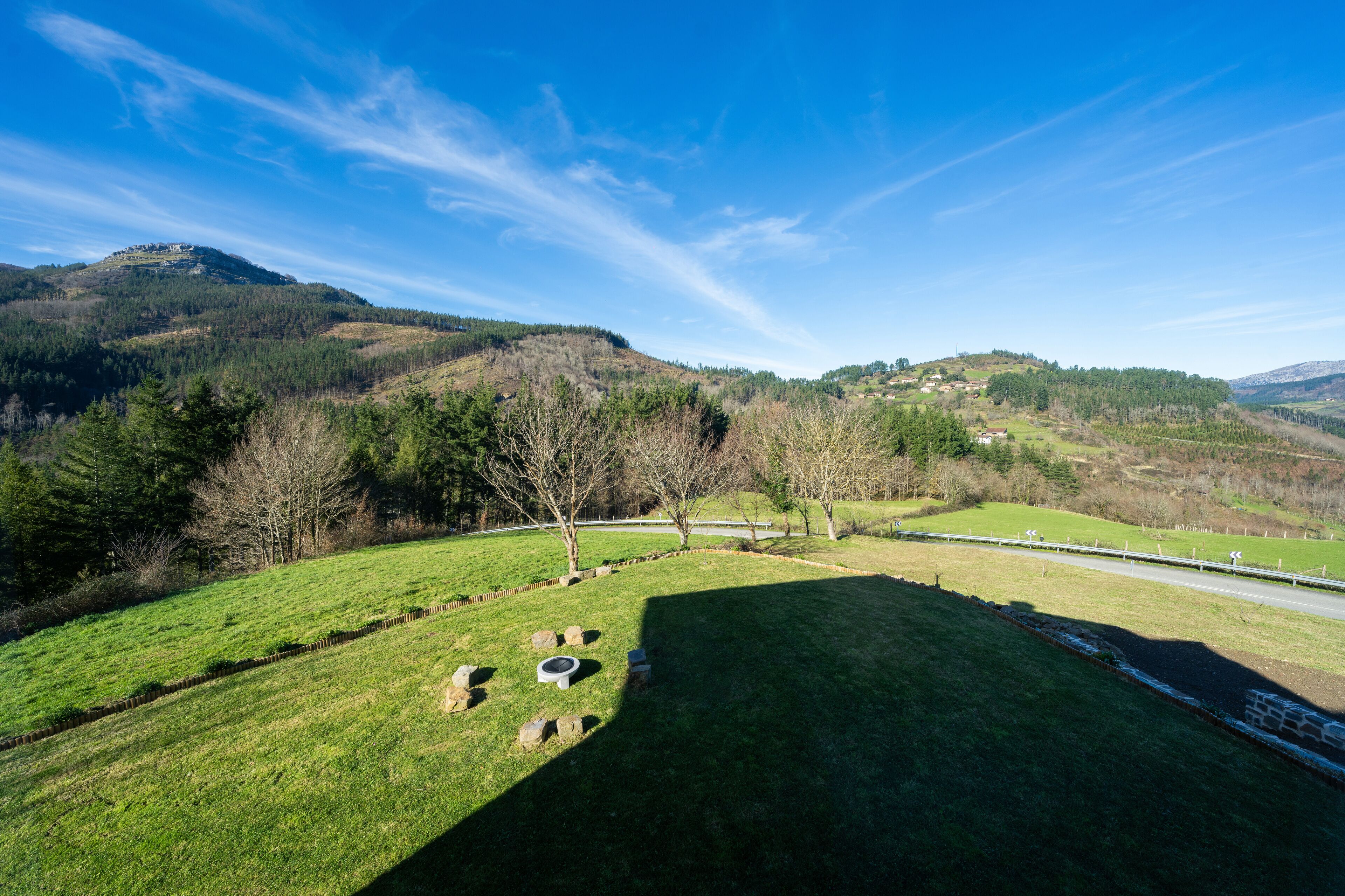 A grassy field with a stone wall, a small pond, and a distant view of a hill with trees and a building.