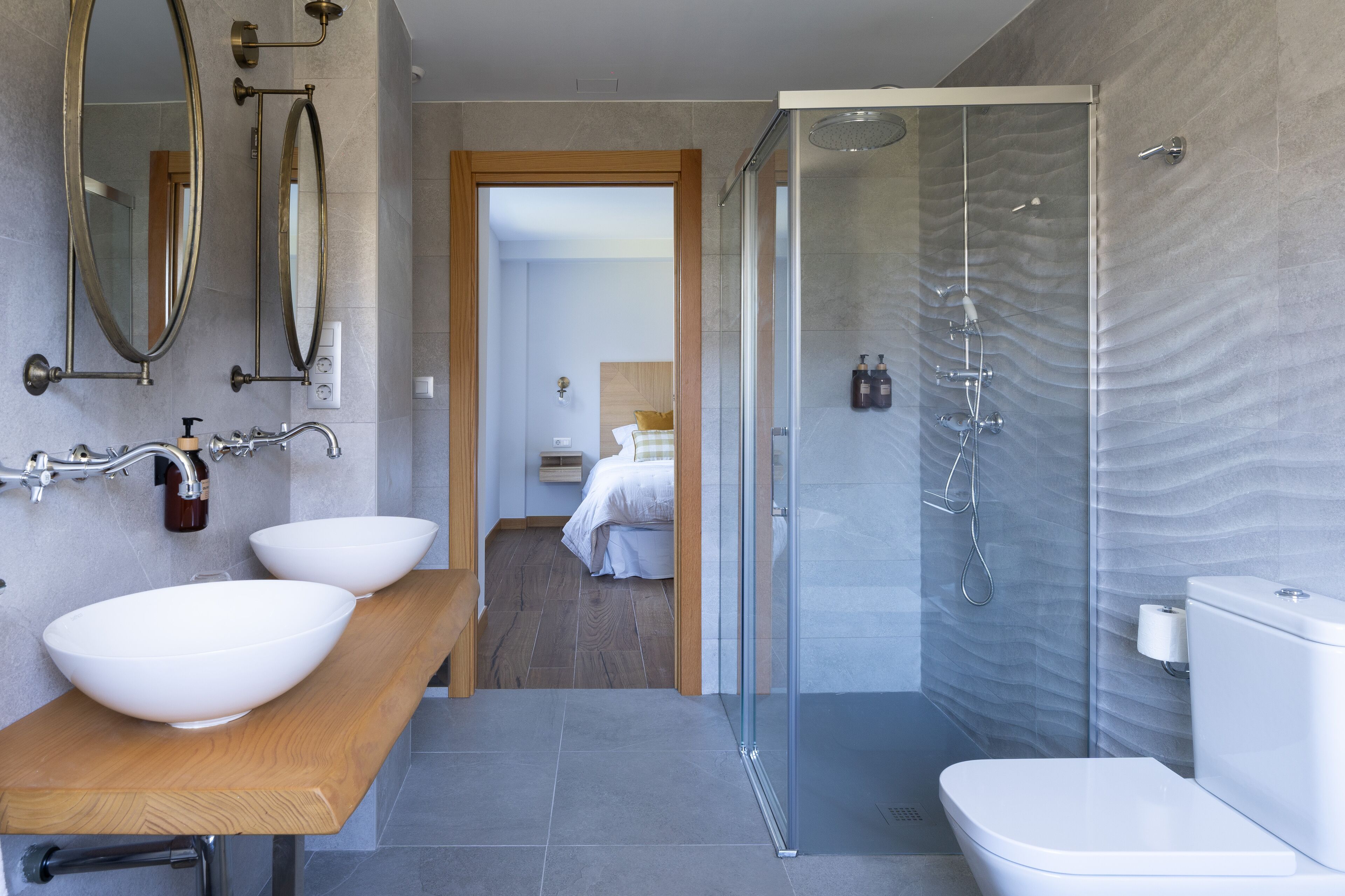 A modern bathroom with a wooden vanity, two large white sinks, a glass shower enclosure, and a white toilet.