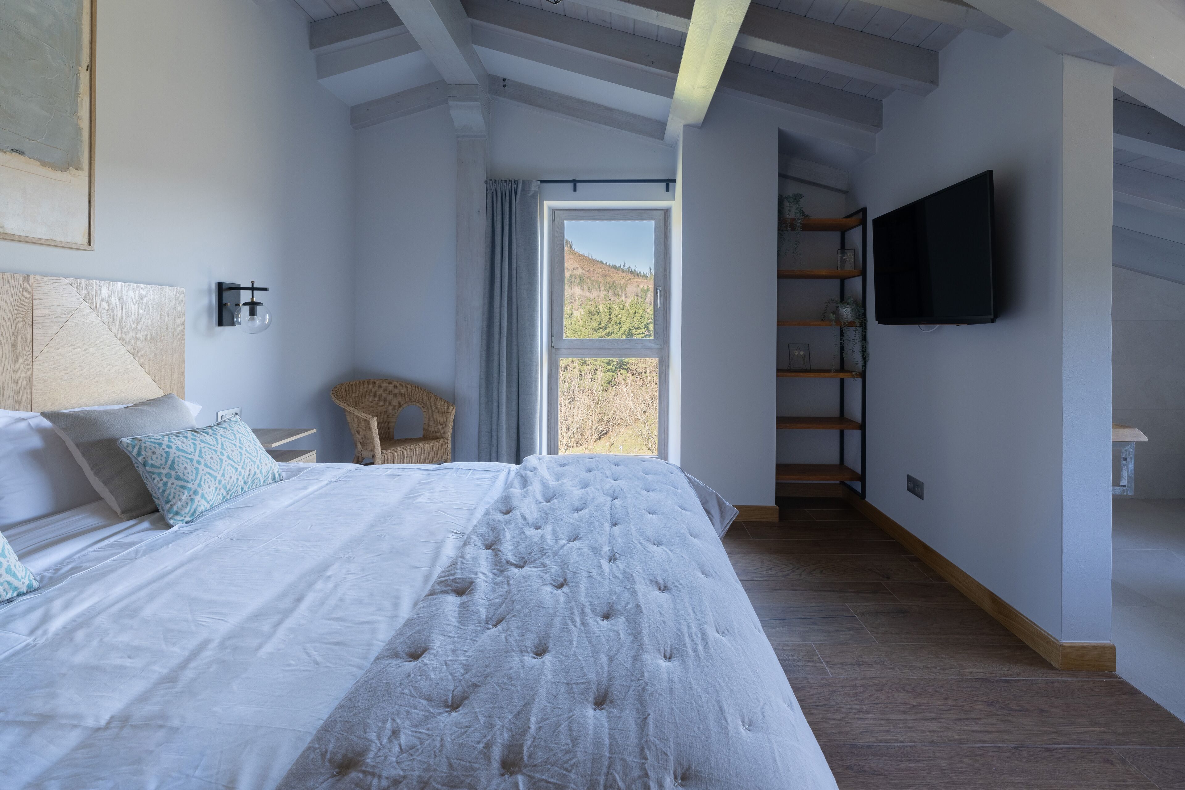 A bedroom with a large bed, a television mounted on the wall, and a view of the outdoors through a window.