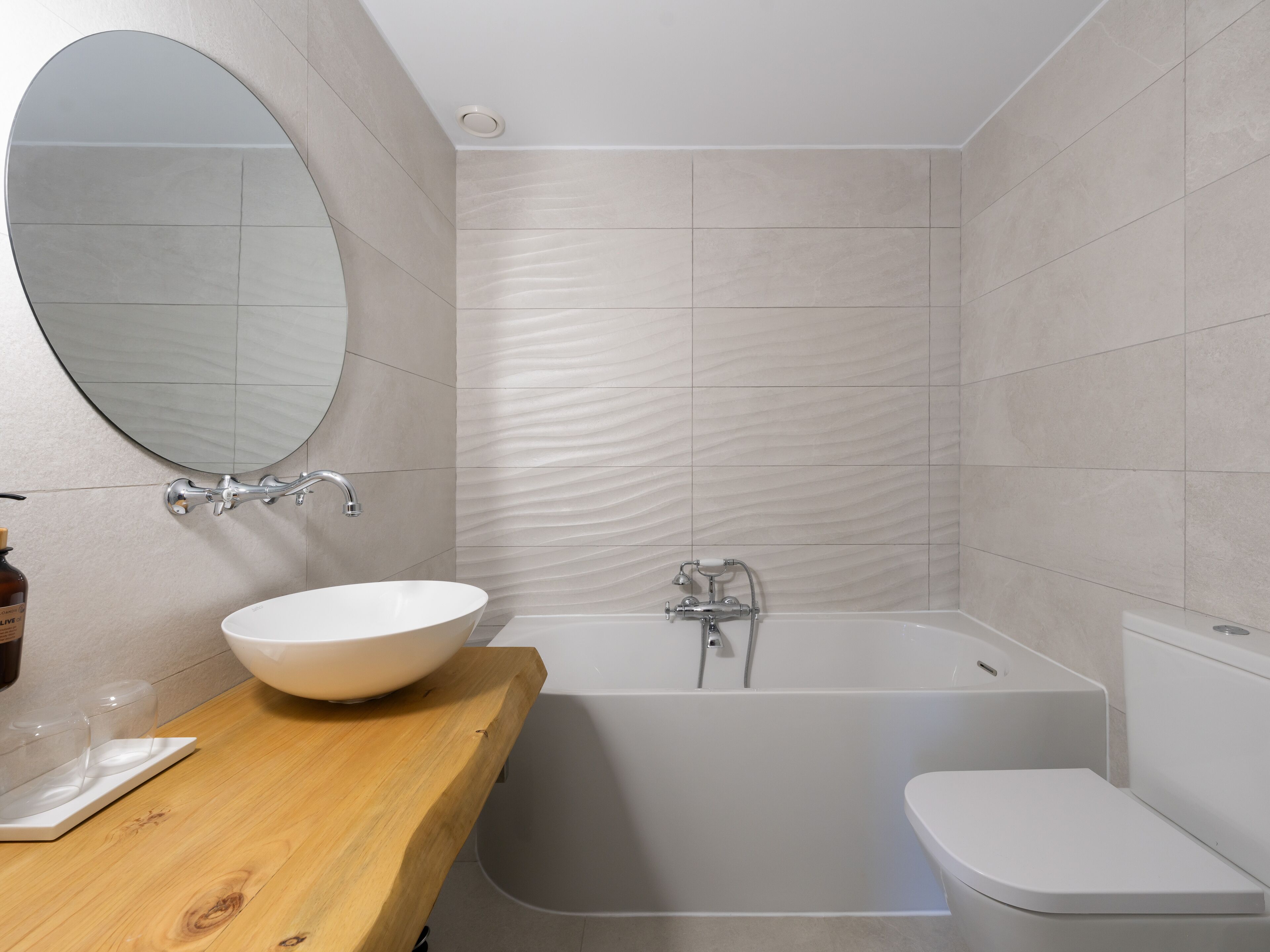 A modern bathroom with a freestanding bathtub, a round mirror, and a wooden vanity.
