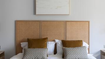 Un lit bien fait, avec deux oreillers, une tête de lit ornée d’un motif tissé et un tableau encadré au-dessus.