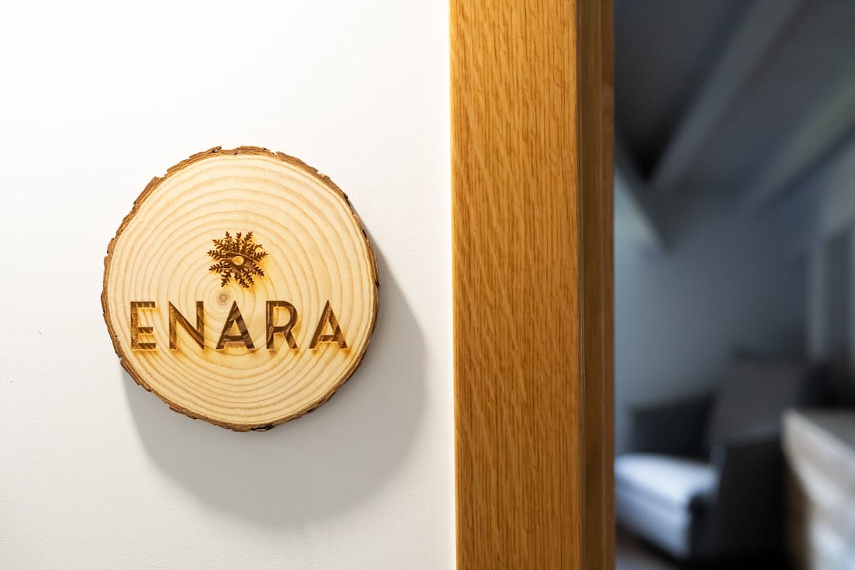 A wooden sign with the word "ENARA" on a white wall.