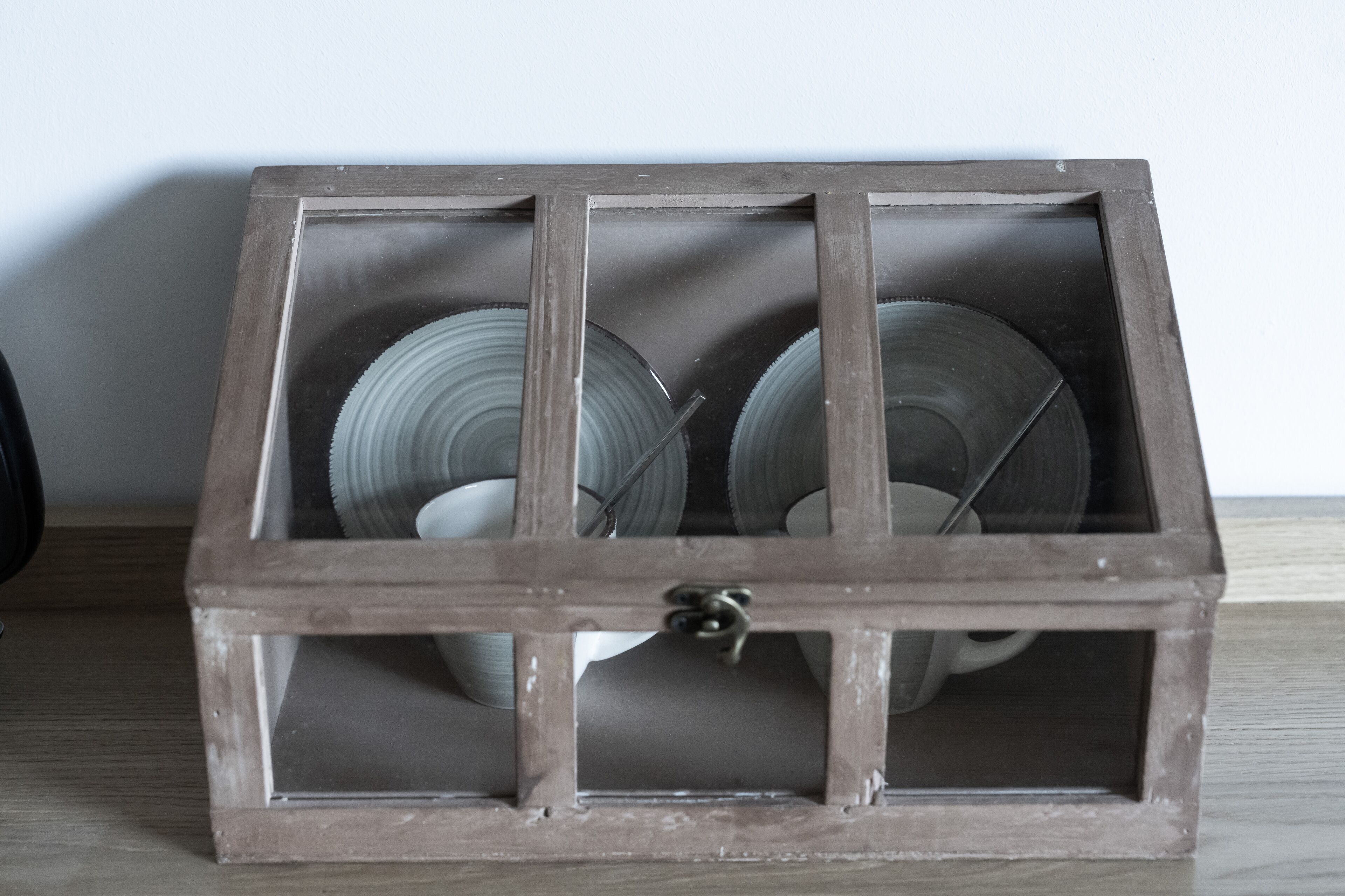 A rustic wooden cabinet with a glass front, containing several glass bowls and a metal spoon.