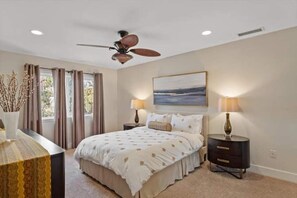 Une chambre à coucher avec un lit, deux tables de chevet, un ventilateur de plafond et un tableau accroché au mur.
