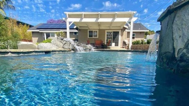 Una piscina con agua cristalina, una casa con porche cubierto y una cascada.