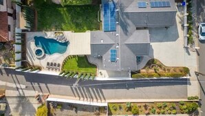Vista aérea de una propiedad residencial con piscina, paneles solares y jardín ajardinado.