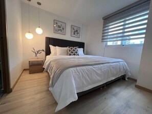 Relax in a serene bedroom with a large bed, framed artworks, and a small nightstand.
