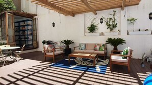 A covered patio area with a wooden ceiling, a blue patterned rug, and a seating arrangement including a sofa and chairs.