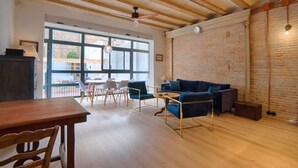 A spacious living area with a wooden ceiling, a brick wall, and a large window providing natural light.