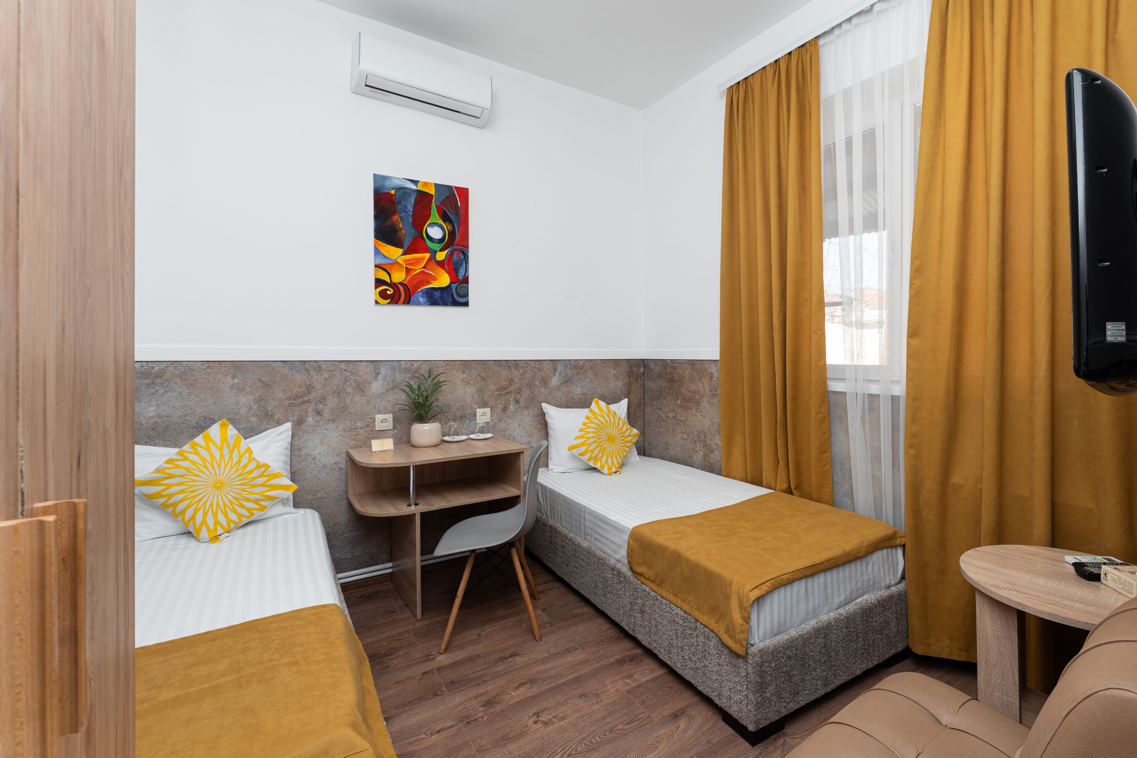 Habitación de hotel con dos camas, un escritorio, una silla, un televisor y una ventana con cortinas.