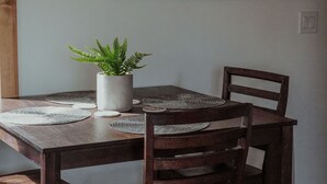Un comedor con una mesa de madera, cuatro sillas, una planta en maceta y un cuadro en la pared.