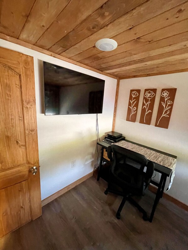 Una habitación con techo de madera, un televisor de pantalla plana en la pared, un escritorio con una silla, y tres paneles decorativos en la pared.