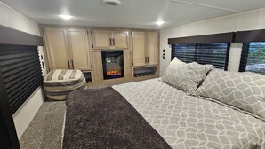 Un dormitorio con cama, zona de estar, chimenea y ventana con persianas.