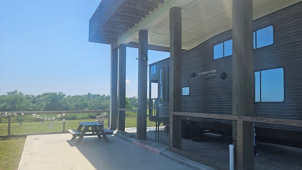 Un edificio moderno con fachada de madera, un patio cubierto con una mesa de picnic y un espacio exterior cercado.