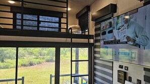 Una habitación con literas, un ventanal grande y un televisor de pared mostrando un anuncio de la Biblia.