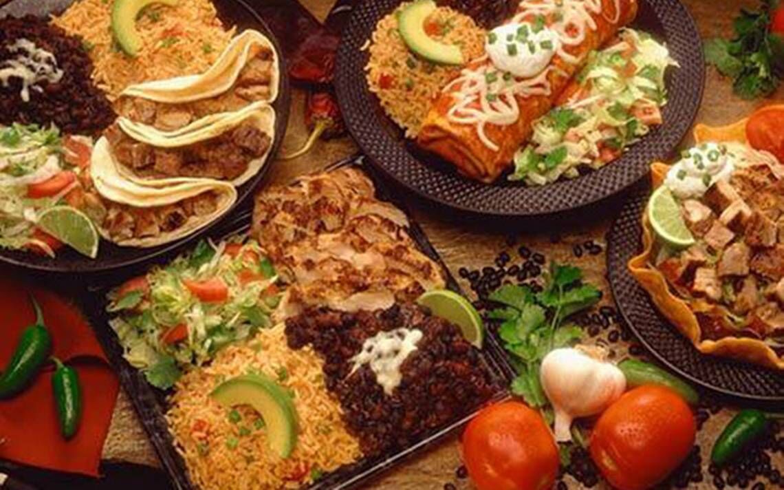 Variedad de platillos mexicanos, como tacos, enchiladas y frijoles, servidos en platos negros.