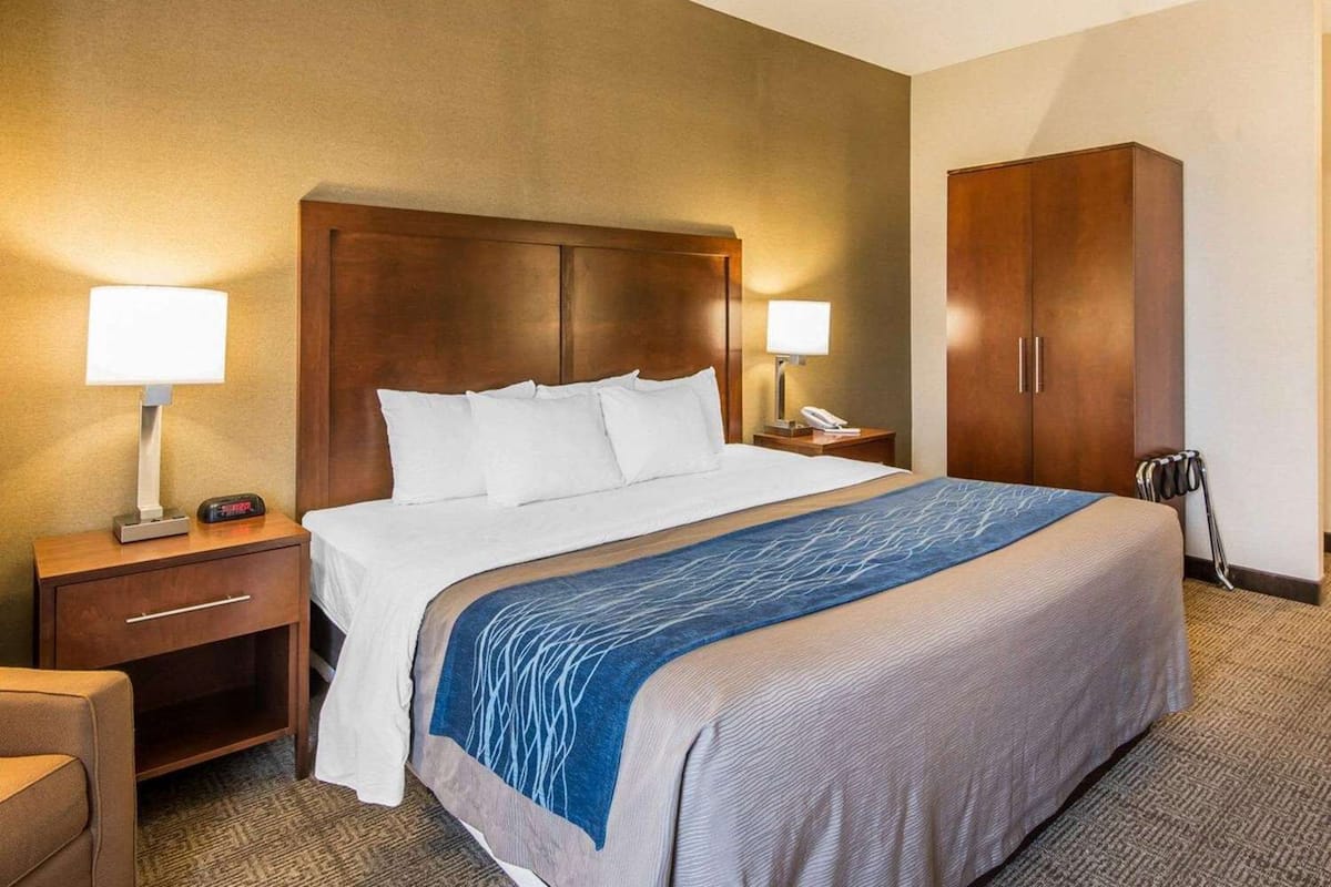 A hotel room with a large bed, two bedside tables with lamps, a wardrobe, and a chair.