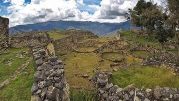 Ancient stone ruins with circular structures, surrounded by grassy terrain and mountains in the background.