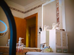 Um banheiro com pia de mármore, espelho, armário com produtos de higiene e porta que dá acesso a outro cômodo.
