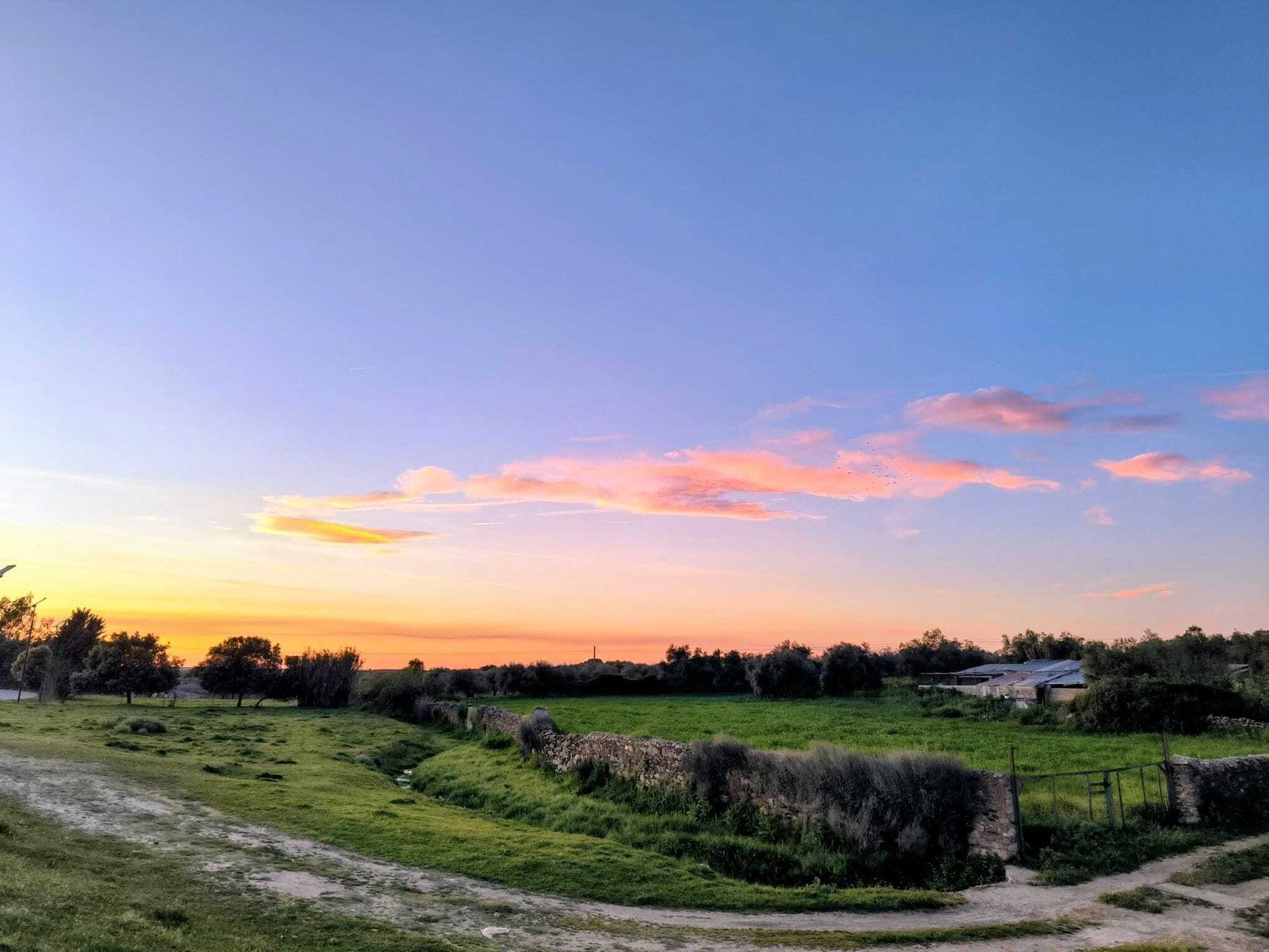 Un paysage rural avec un chemin de terre, des murs de pierre et un bâtiment visible au loin.