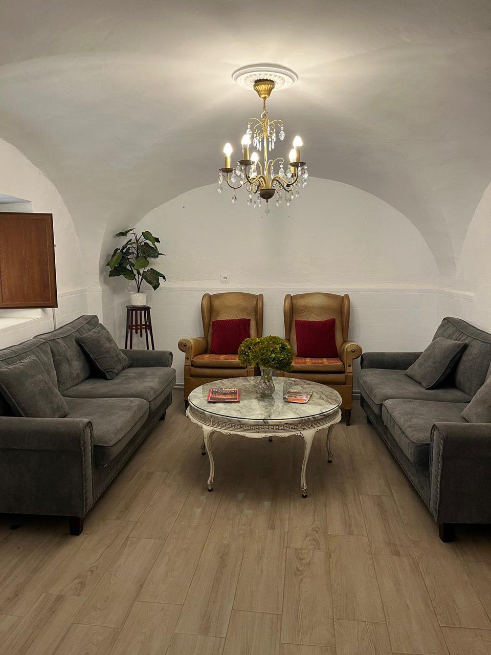Een gezellige woonkamer met een kroonluchter, twee fauteuils, een bank en een kleine tafel met een plant.
