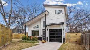 Een modern huis met twee verdiepingen, een garage, omheind door een houten schutting en met een kleine tuin.