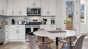 Een moderne keuken met witte kasten, een RVS magnetron, een inbouwoven en een ronde eettafel met vier stoelen.