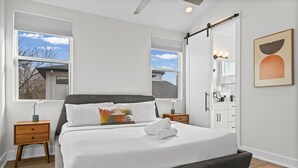 Een slaapkamer met een groot bed, twee nachtkastjes, een kaptafel, een spiegel en een raam met jaloezieën.