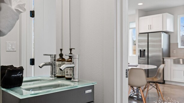 Een moderne keuken met een roestvrijstalen koelkast, een glazen spoelbak met twee zeepdispensers, en een eethoek met een ronde tafel en stoelen.