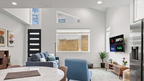 Een moderne woonkamer met een hoge plafond, een groot raam, een flatscreen-tv, een koelkast en een eethoek.