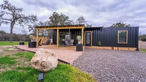 En moderne udendørs patio med pergola, siddepladser og en stor klippefortolkning.