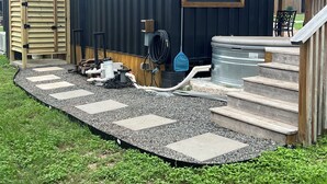 En modulopbygget bygning med et overdækket udeområde, trapper op til en terrasse og et vandelement.