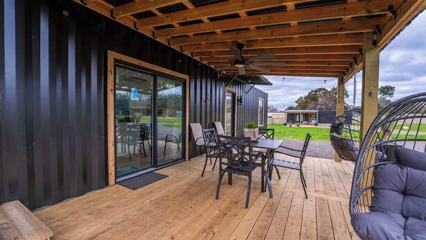 En overdækket terrasse med træterrasse, et bord og stole, samt en hængestol.