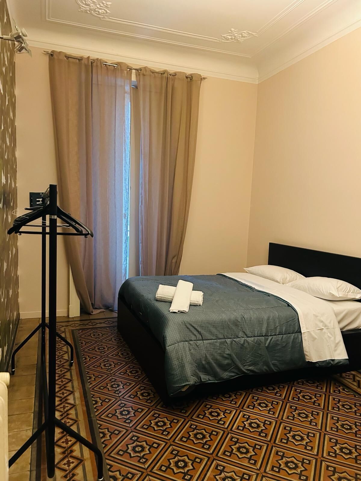 A hotel room with a bed, a standing lamp, and patterned floor tiles.