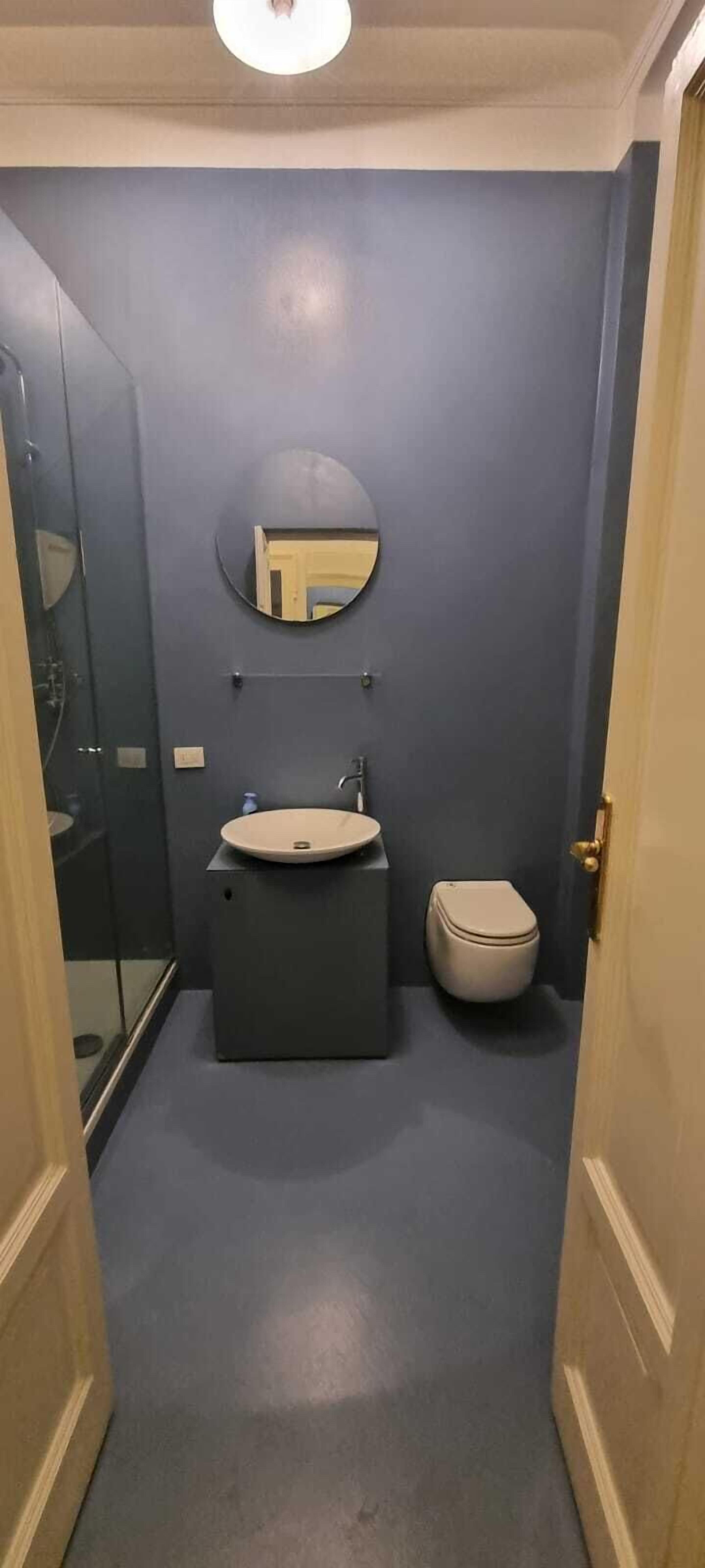 A narrow bathroom with a round mirror, a sink, and a toilet.
