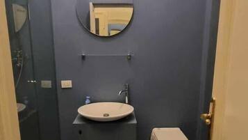 A narrow bathroom with a round mirror, a sink, and a toilet.